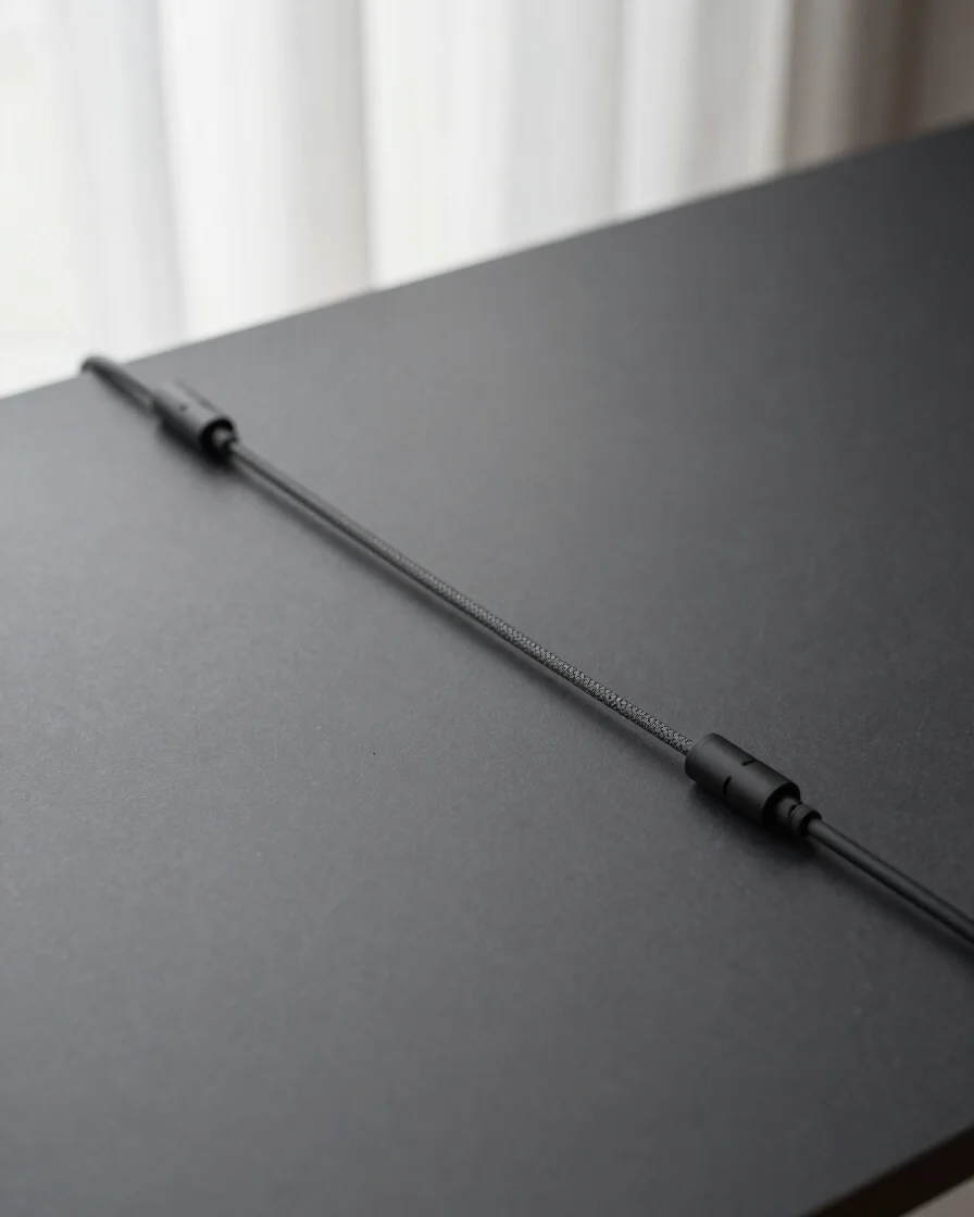 Minimalist desk setup, top-down view, matte charcoal surfaces, woven cables, soft diffused window light, crisp detail, 3